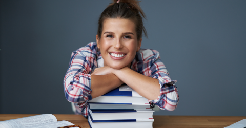 Jonge meid met haar armen op een stapel boeken achter haar bureau